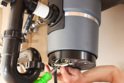 Man using tool to repair a garbage disposal.