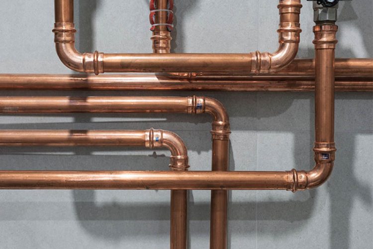 Closeup of copper plumbing system pipes running along wall.