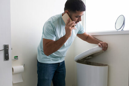 Man on the phone while lifting the tank lid to a toilet to check for problems.