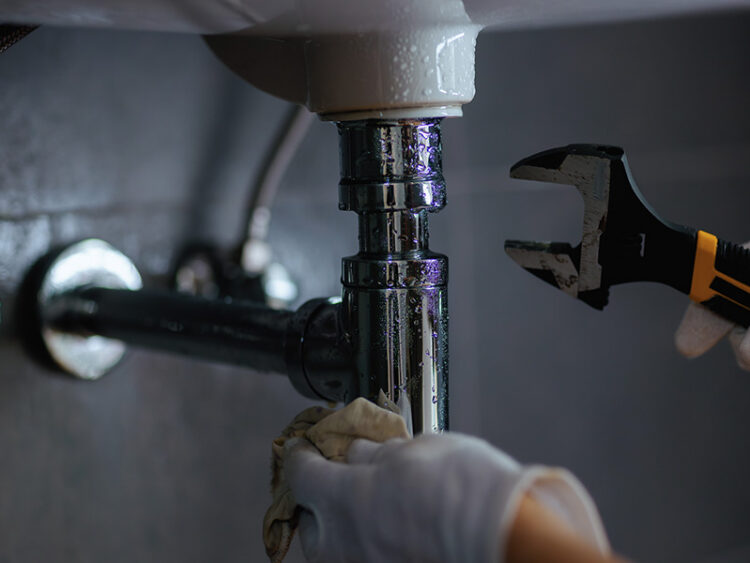Plumber using a wrench to remove a tailpiece under a sink.
