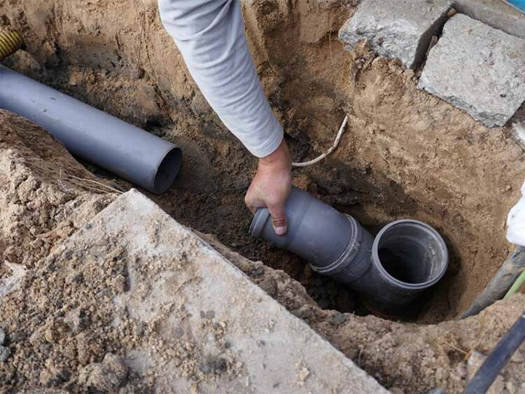 Plumber laying new PVC sewer line in trench.