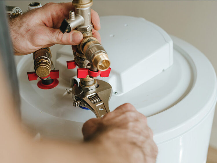 Plumber using wrench to tighten new fitting on water heater pipe.
