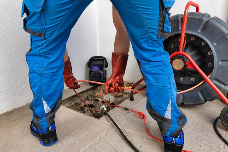 Plumber using hydro jetting equipment to clean plumbing line.