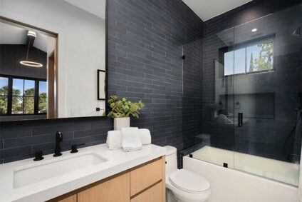 Modern bathroom with dark color tiles and light wood and porcelain vanity.
