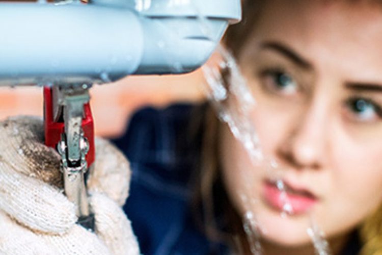 woman using wrench on leaky pipe