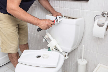 Man holding a wrench and looking into the tank of a toilet, trying to fix it.