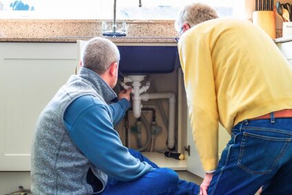 2 men looking at plumbing lines under kitchen sink.
