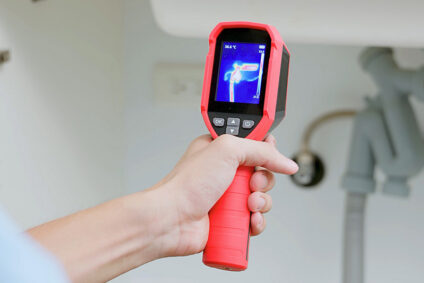 Plumber holding thermal imaging tool to detect leak under bathroom sink.