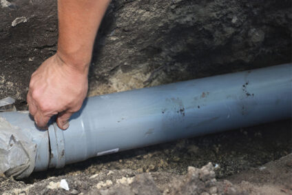 Man placing a piece of new sewer line pipe into trench.
