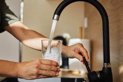 Man filling a glass with water from a kitchen sink.