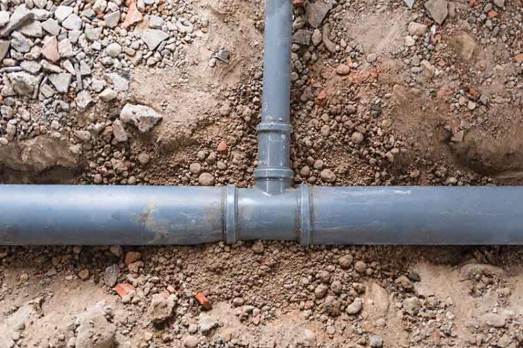 T-shaped gray sewer pipes surrounded by dirt.