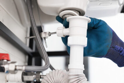 Plumber removing tailpiece from under a kitchen sink to clean the drain.